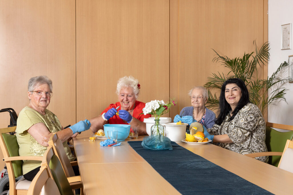 Bewohnerinnen bereiten mit einer Mitarbeiterin einen Obstsalat zu.