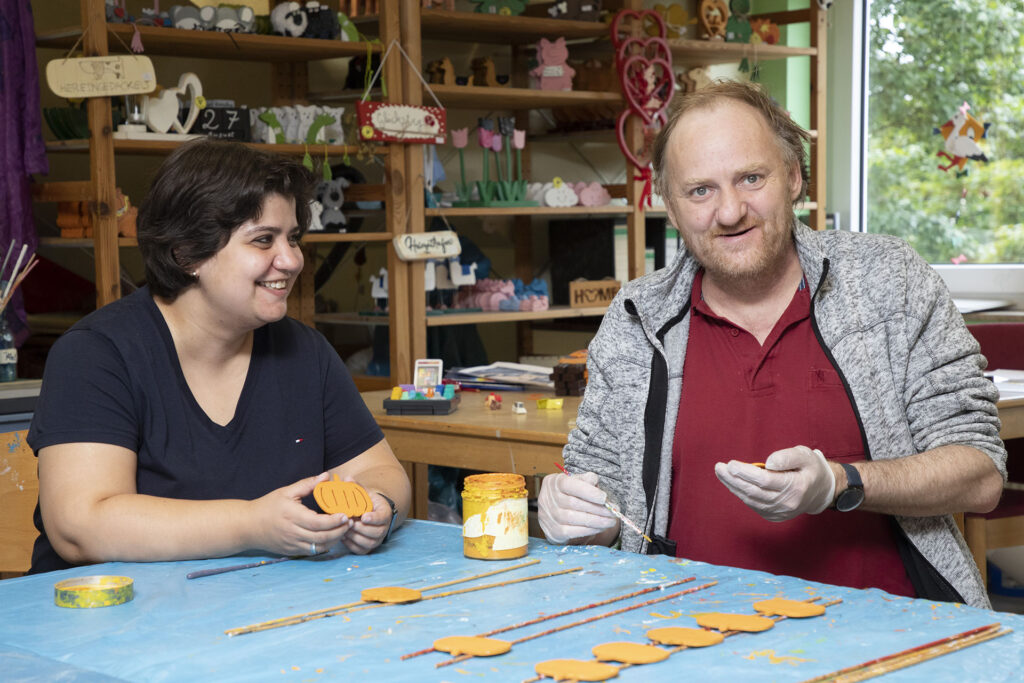 Eine Mitarbeiterin und ein Bewohner fertigen in der Ergotherapie Holzdekorationen an.