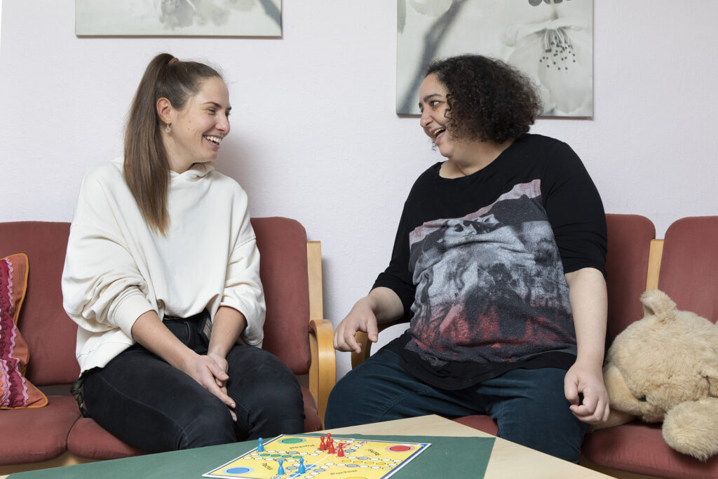 Eine Mitarbeiterin und eine Bewohnerin spielen ein Brettspiel und unterhalten sich.