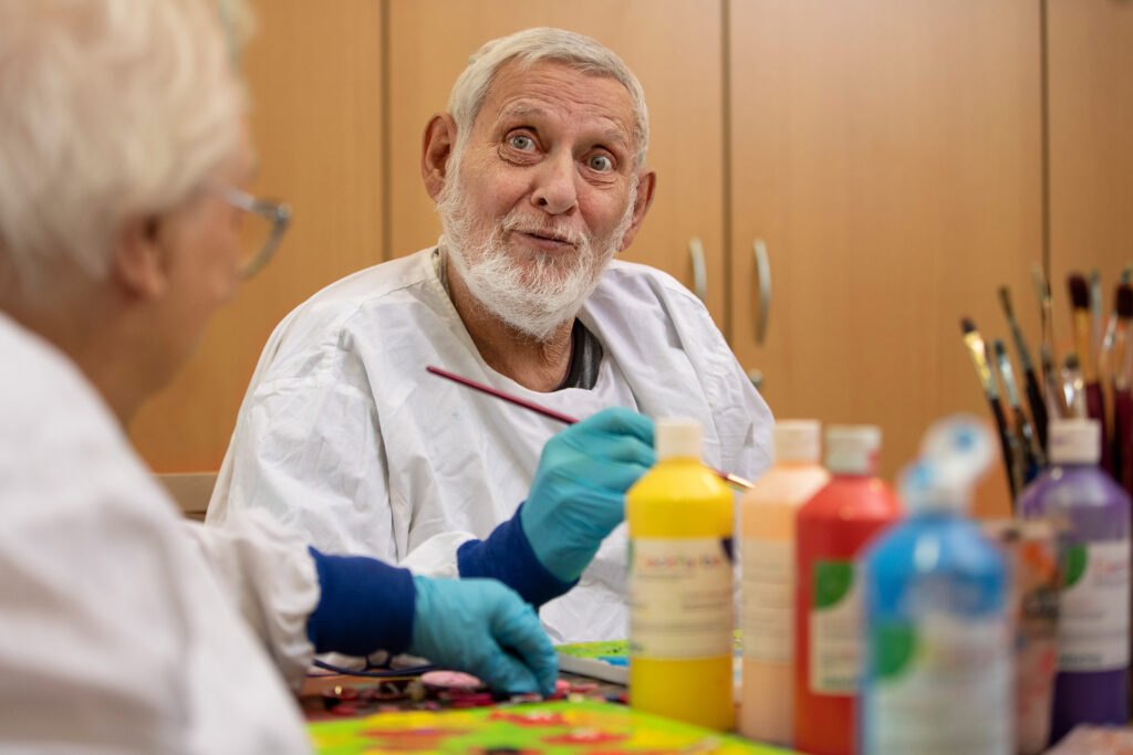 Ein Bewohner, der an der Kreativgruppe teilnimmt, lächelt in die Kamera.