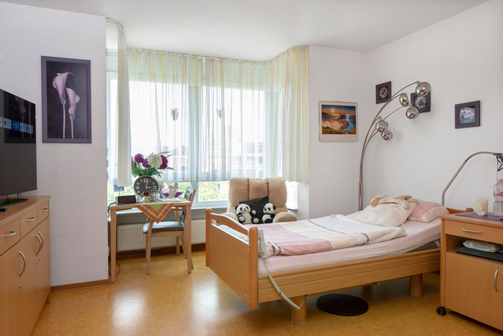 Blick in ein Bewohnerzimmer: Durch das große Fenster fällt viel Tageslicht. Nebem dem Mobiliar ist viel Platz für persönliche Gegenstände.