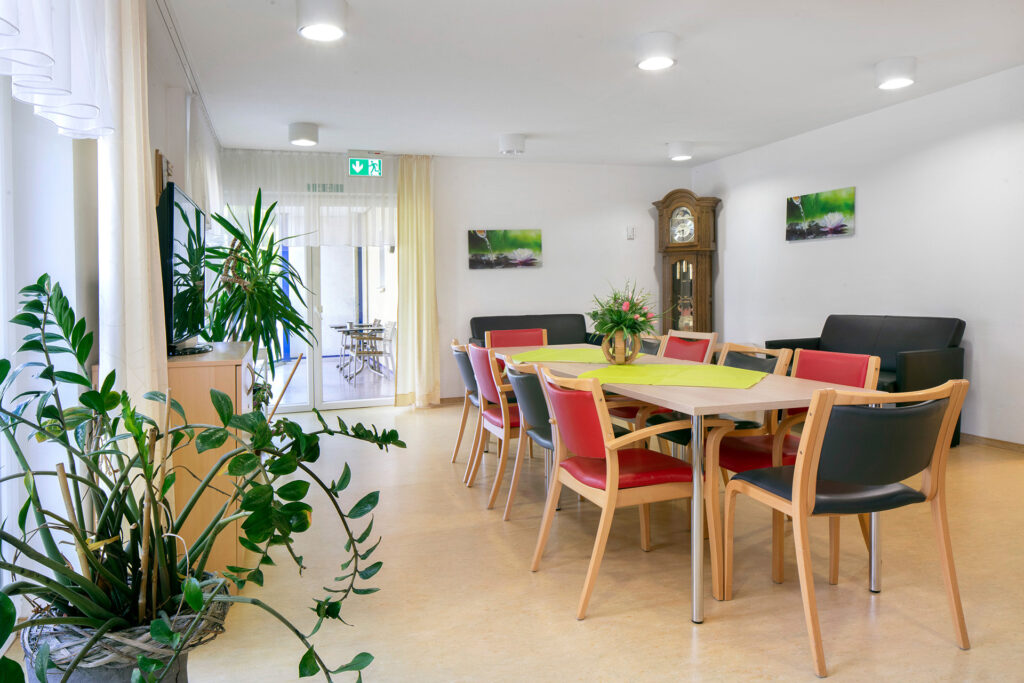 Blick in einen Aufenthaltsraum, der unter anderem mit einer antiken Standuhr und Grünpflanzen dekoriert ist.