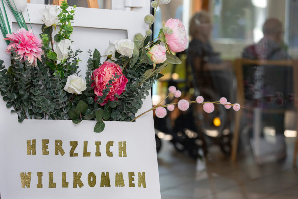 Auf einem großen, mit Blumen geschmückten Schild im Eingangsbereich steht "Herzlich Willkommen".
