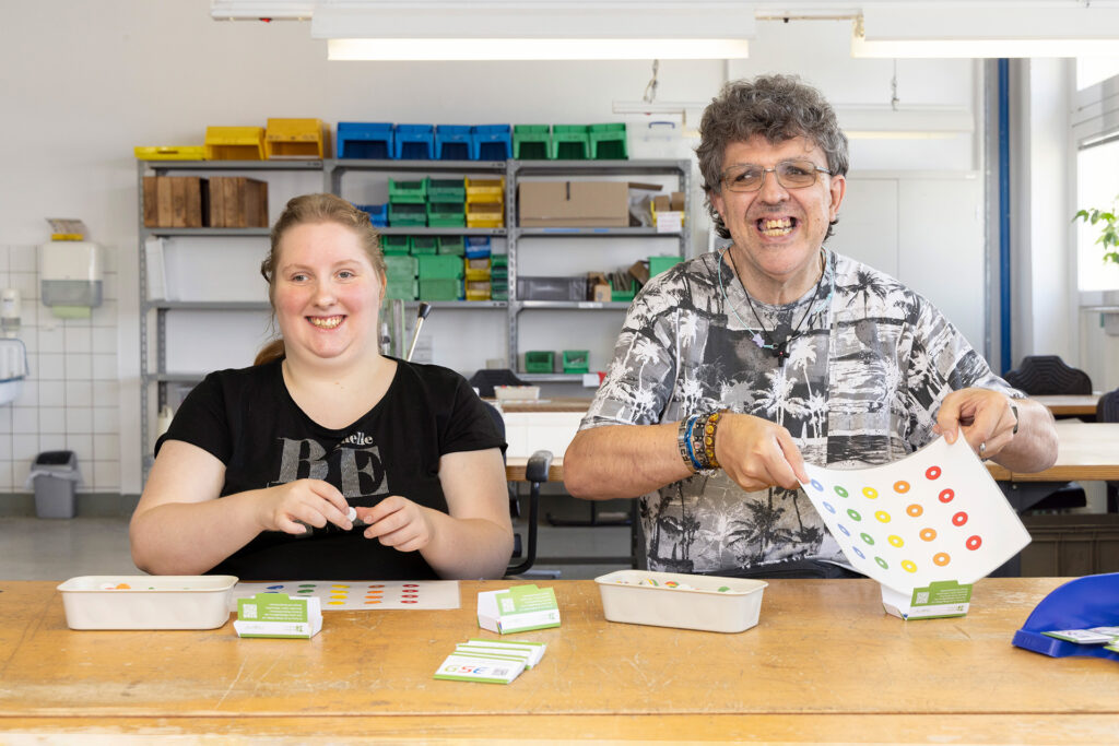 Zwei Werkstattmitarbeitende stellen Hand in Hand Werbemittel zusammen.