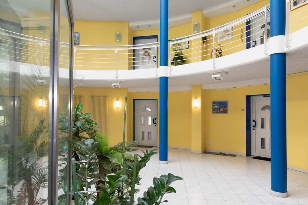 Blick in das Treppenhaus der Wohnanlage Drostenbusch: Durch den Rundbau ist das Treppenhaus sehr geräumig. Durch Oberlichter fällt Tageslicht in diesen Bereich, die Wände sind gelb gestrichen.