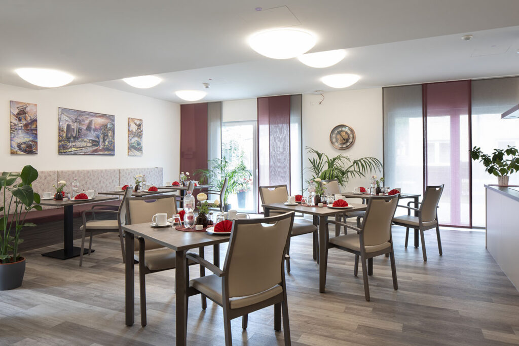 Blick in den Aufenthalts- und Speiseraum, in den durch bodentiefe Fenster viel Tageslicht fällt.