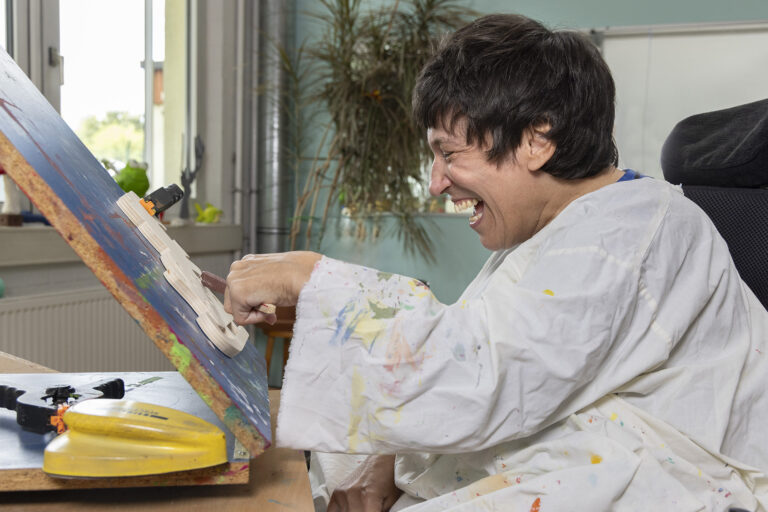 Ein Werkstattmitarbeiter sitzt vor einem Aufsteller und gestaltet ein Werkstück aus Holz.