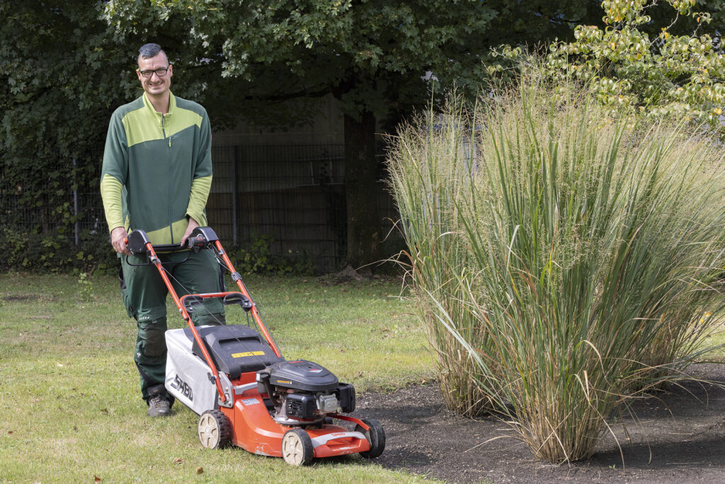 Ein Werkstattmitarbeiter mäht mit einem Rasenmäher den Außenbereich der GSE-Werkstatt Borbeck