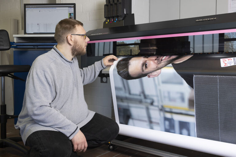 In der Druckerei kontrolliert ein Werkstattmitarbeiter den Druck an der Druckmaschine.