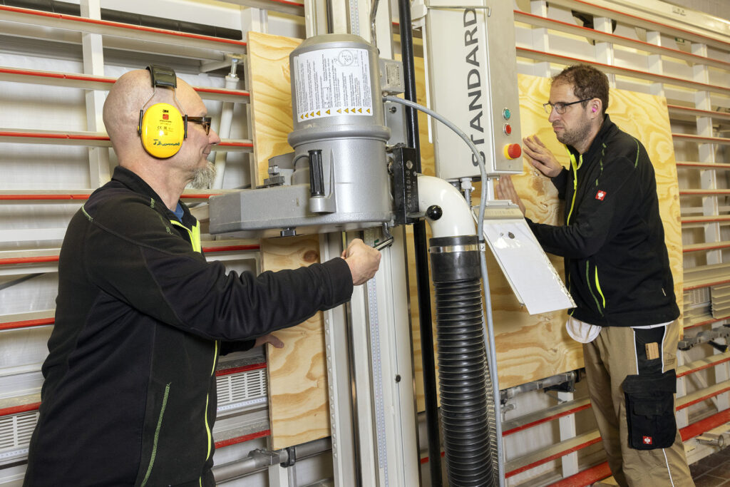 Zwei Werkstattmitarbeiter der Schreinerei in der Werkstatt Frillendorf B sägen an einer Maschine eine Platte für den Möbelbau.