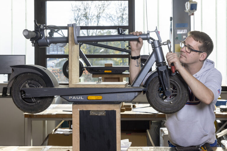 Ein Werkstattmitarbeiter verschraubt ein Teil an einem aufgebockten E-Scooter.