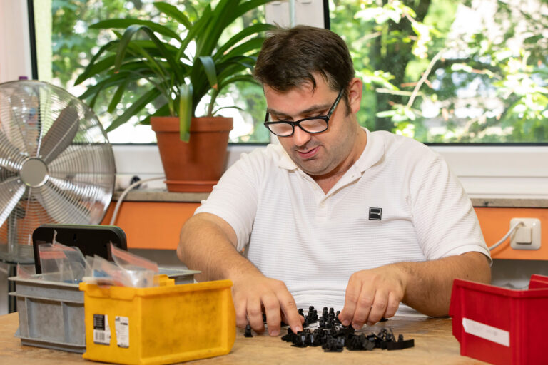 Ein Werkstattmitarbeiter legt konzentriert Geräteteile für die weiteren Arbeitsgänge zusammen.