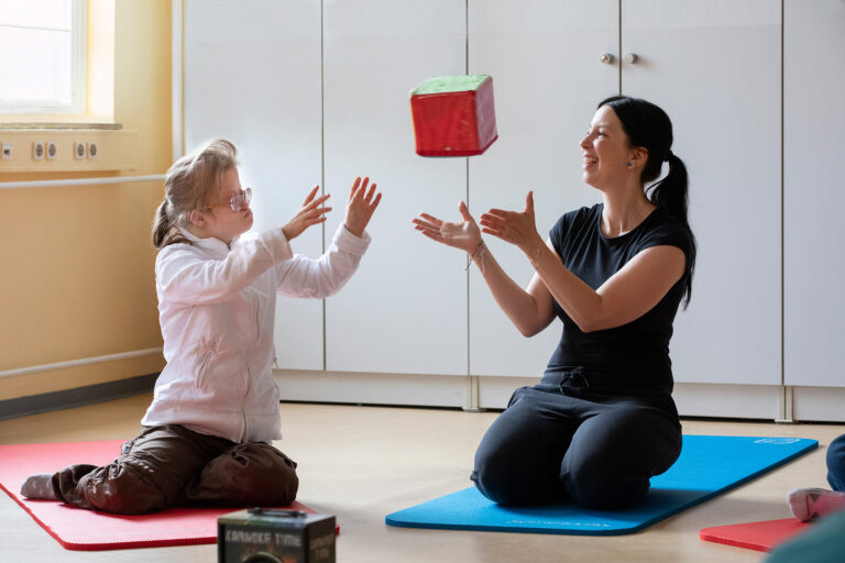 Im Rahmen einer Bewegungsrunde werfen sich eine GSE-Mitarbeitende und eine Teilnehmerin einen Stoffwürfel zu.