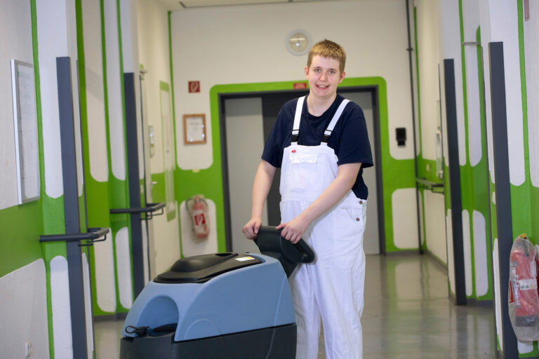 Ein Teilnehmer fährt eine Reinigungsmaschine über einen Gang in der GSE-Werkstatt Kray.