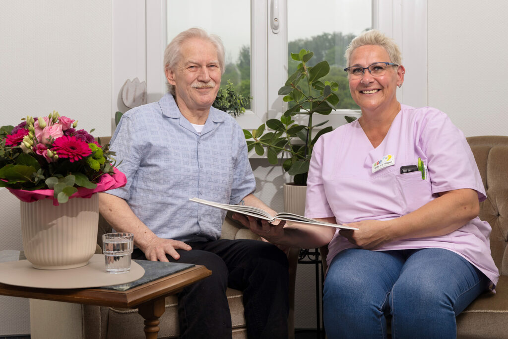Eine Mitarbeiterin und ein Bewohner haben sich gemeinsam ein Album angeschaut und lachen in die Kamera.