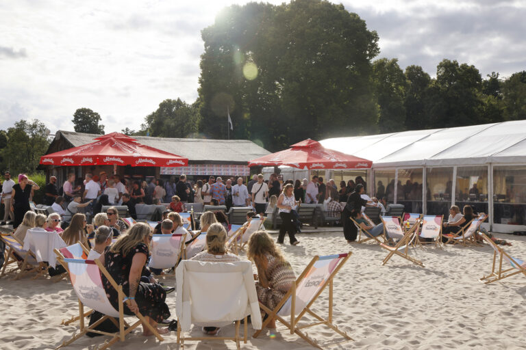 Viele Mitarbeitenden sitzen in Liegestühlen am Seaside Beach Baldeney. Im Hintergrund sieht man Sonnenschirme und viele andere Personen, die an der GSE-Strandbar stehen.