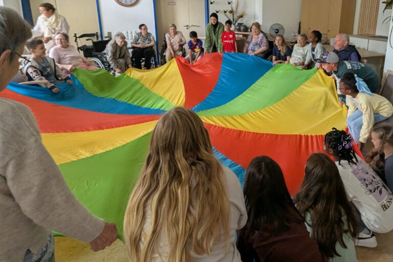 Viele Kinder und Bewohner stehen oder sitzen rund um ein buntes Schwungtuch und sind in Aktion.